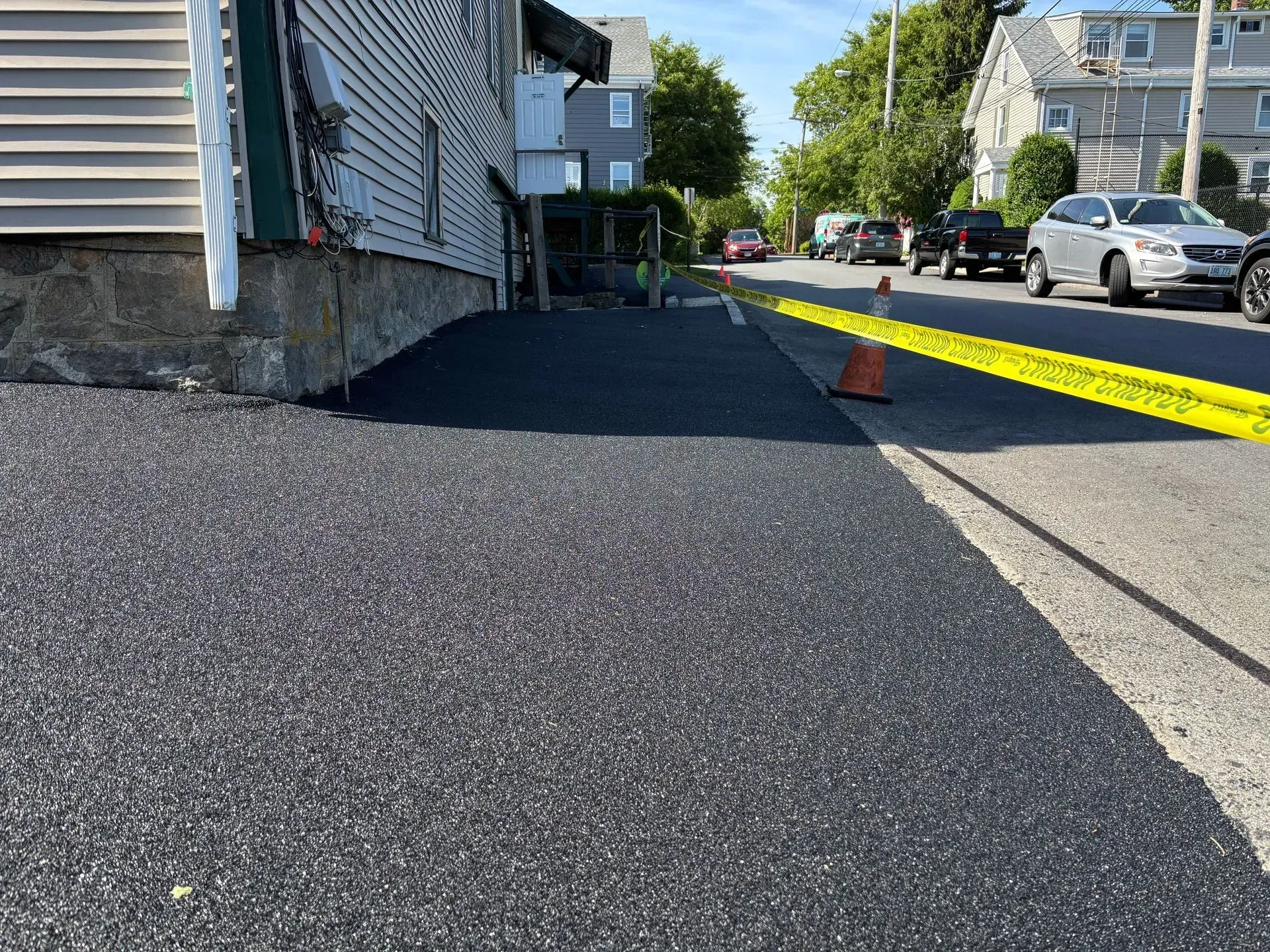 Asphalt paving on a street next to a building. Yellow caution tape and traffic cones mark the work zone.