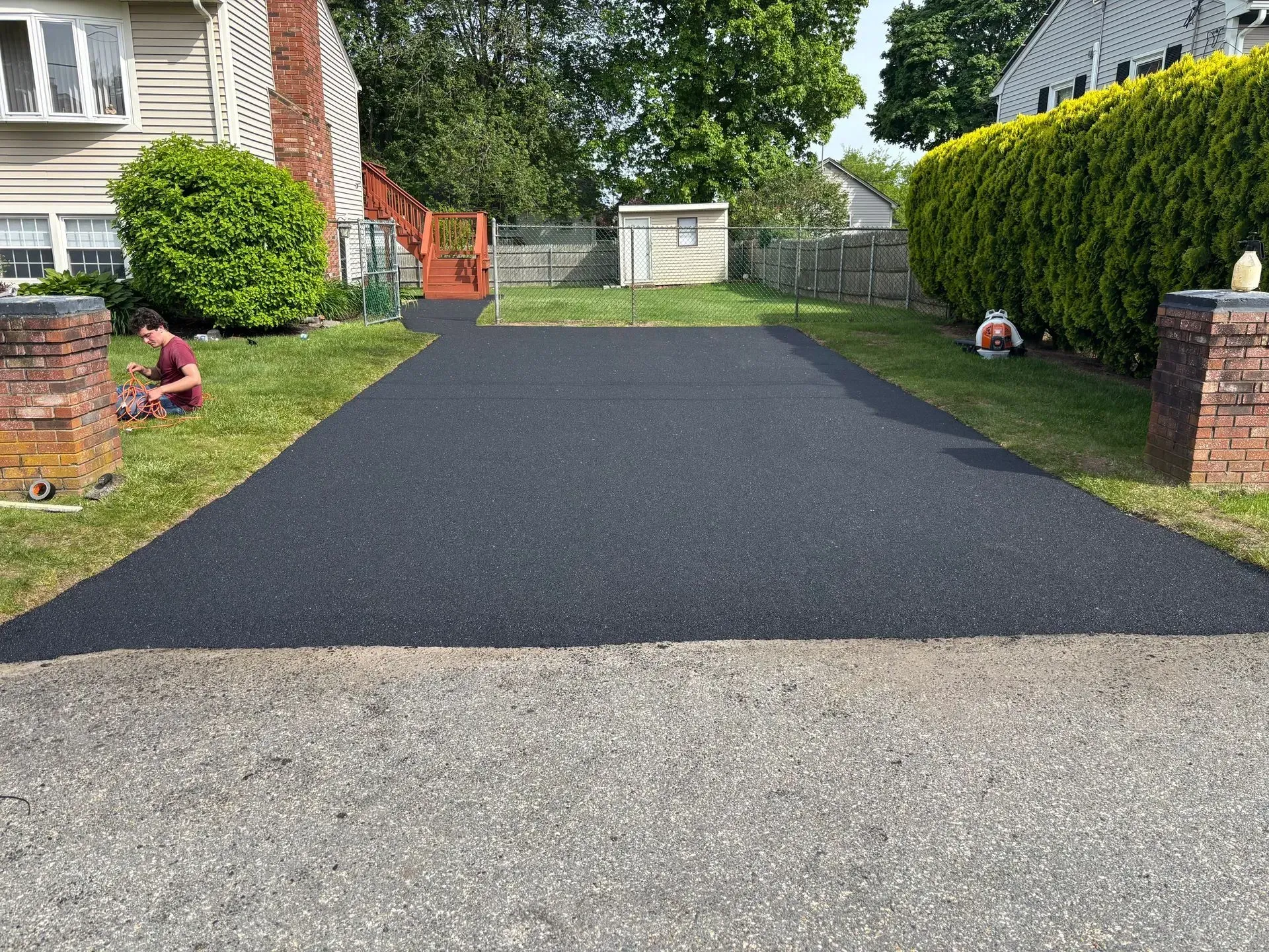 Newly paved black asphalt driveway between grassy lawns, workers nearby.