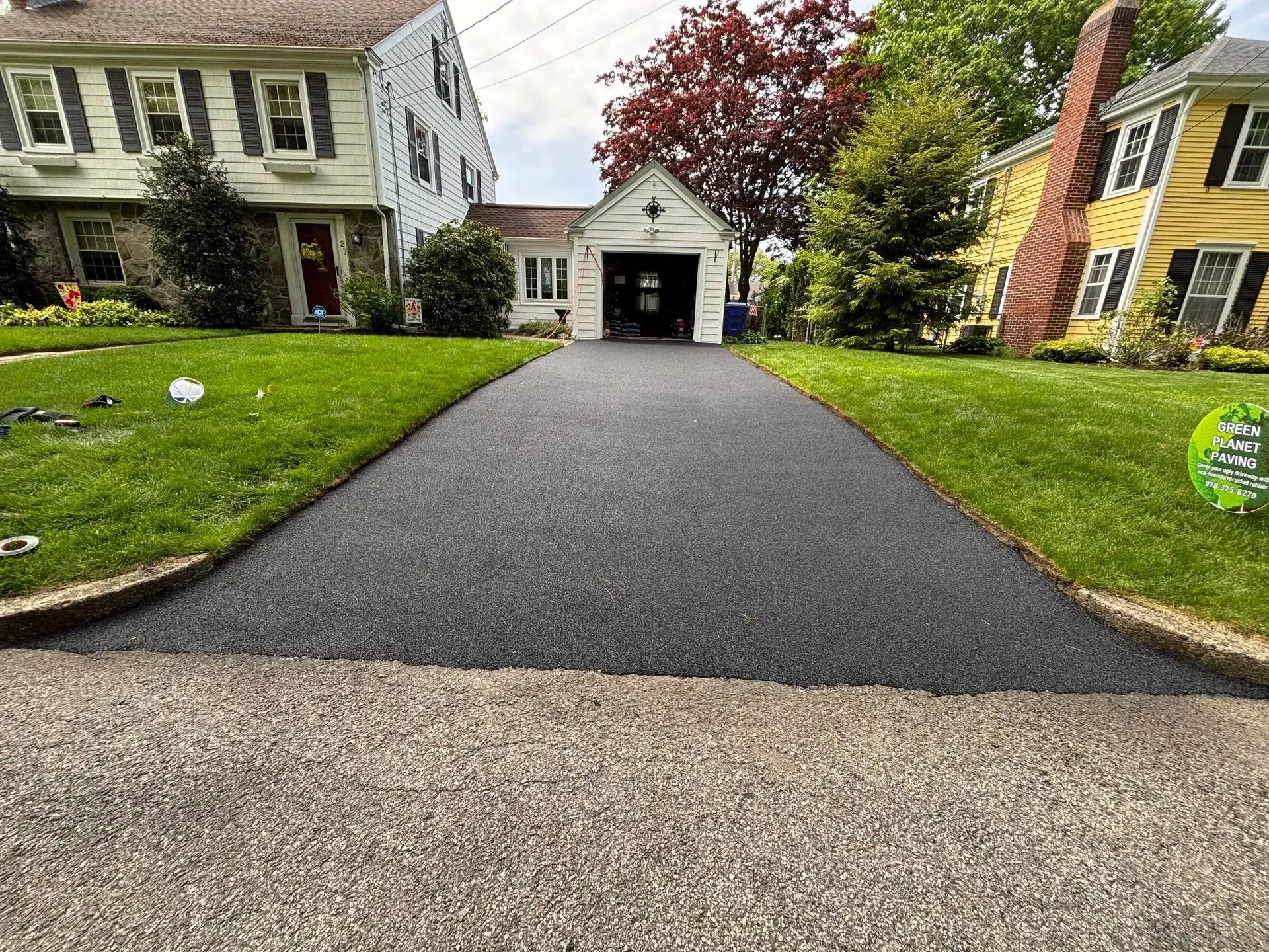 Paved driveway leading to a garage between two houses, green lawns on either side.