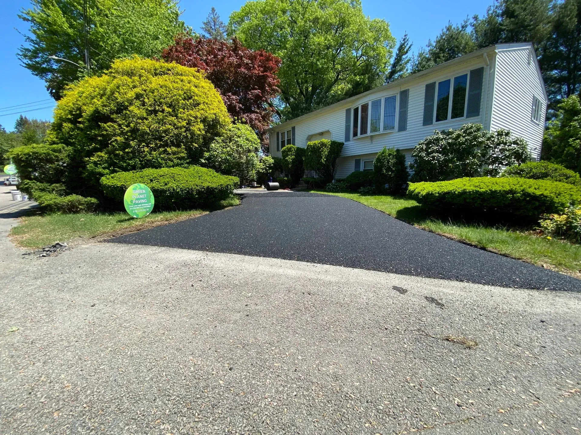 Freshly paved black asphalt driveway leading to a white house with landscaping.