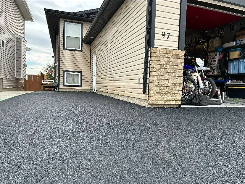 Dark asphalt driveway in front of a tan two-story house with open garage and motorcycle.