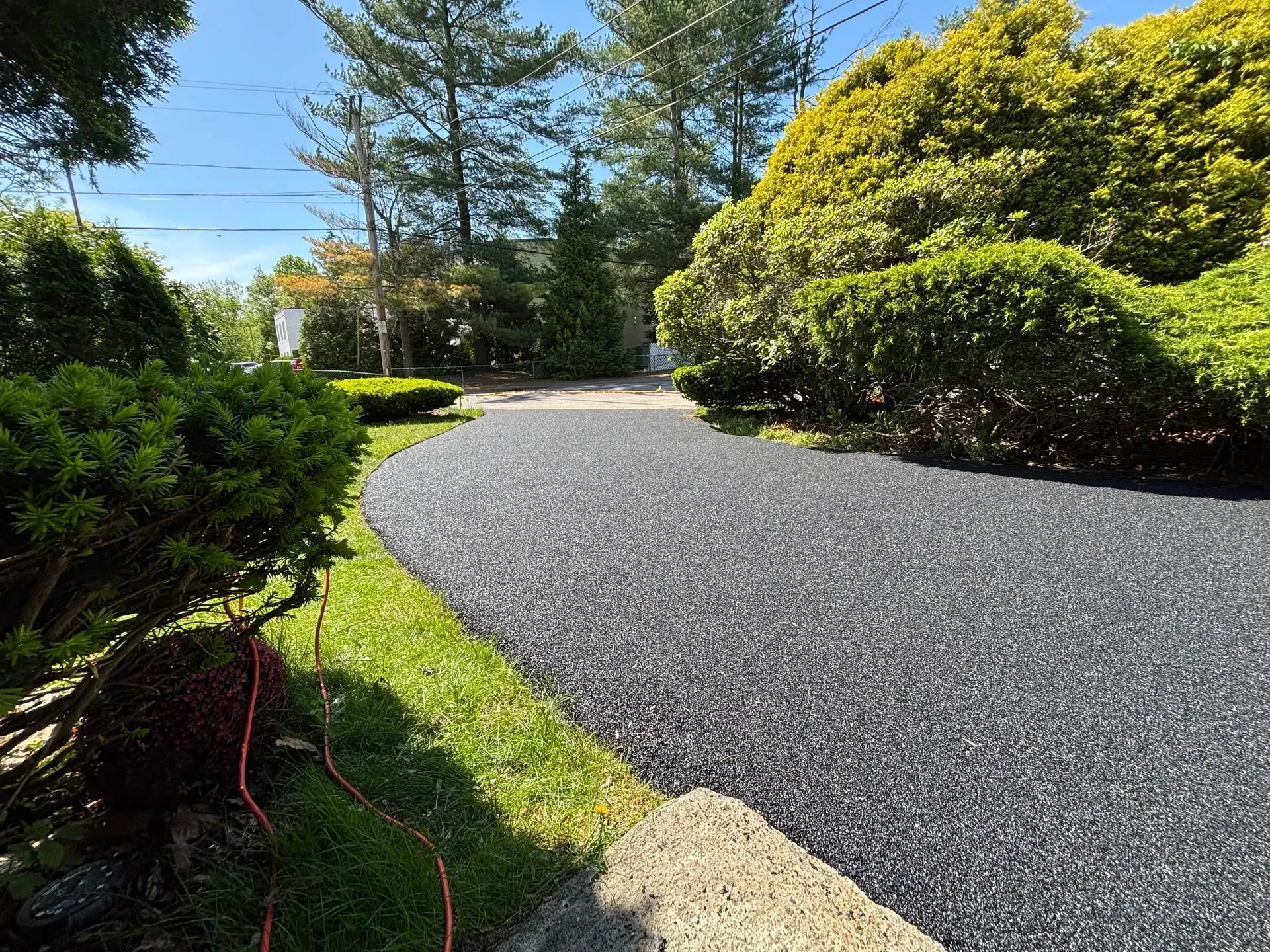 Dark gray gravel driveway curves through a green yard, surrounded by bushes and trees.