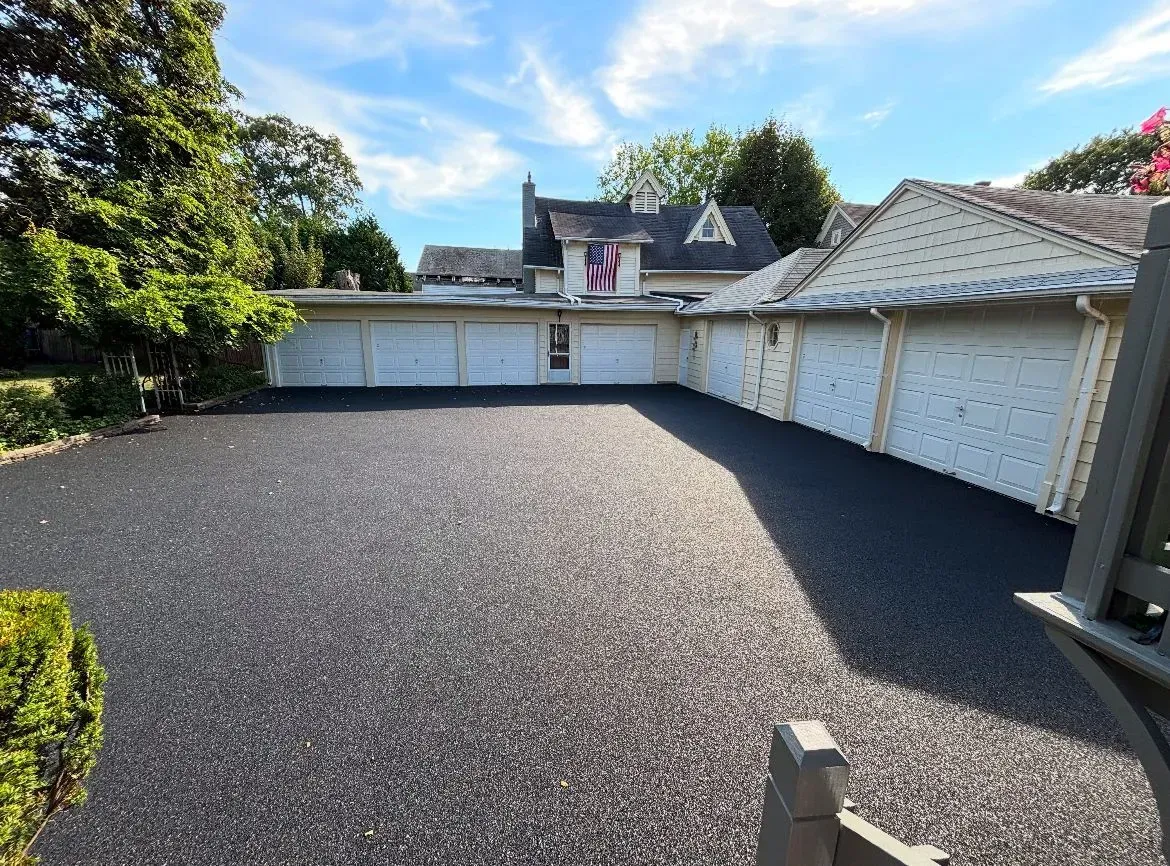 Black asphalt driveway in front of a house with multiple garage doors.