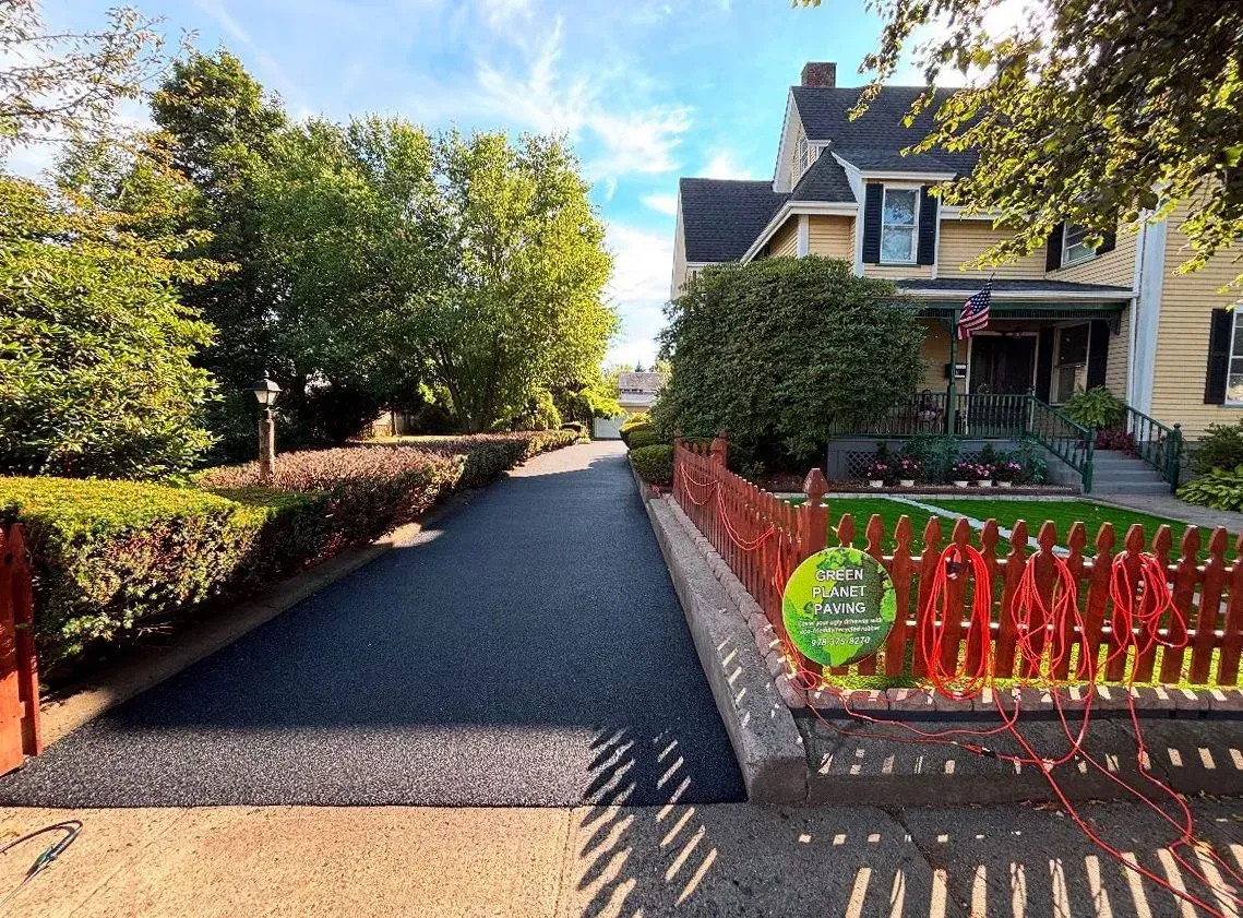 Long driveway leading to a yellow house with a red picket fence and manicured lawn.