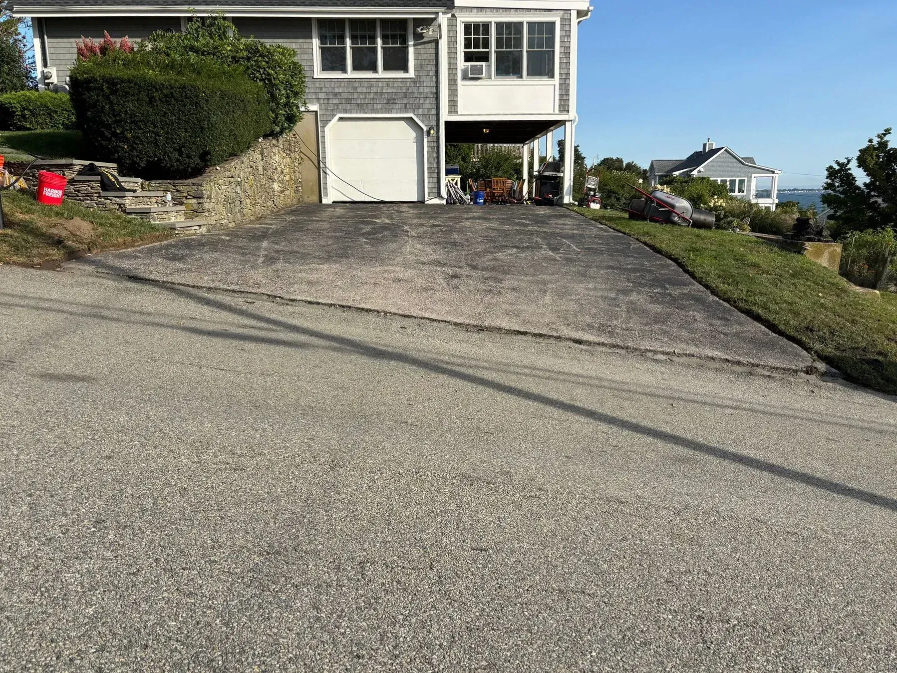 A house with a driveway. The driveway is gray and leads to a garage. There's green grass and bushes.