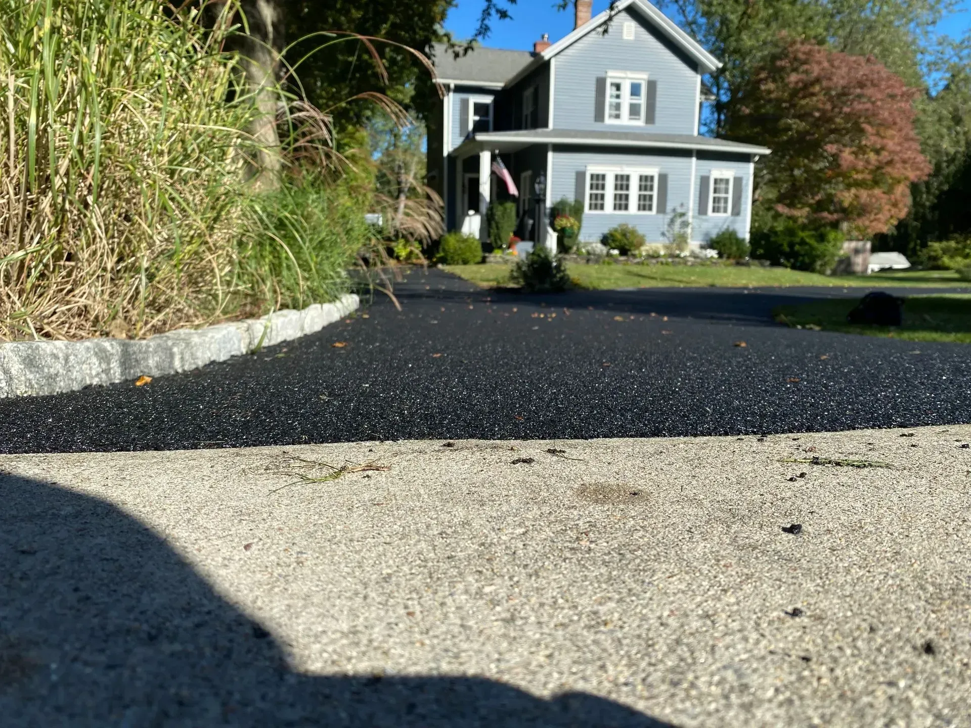 Freshly paved asphalt driveway in front of a gray house with white trim and a flagpole.