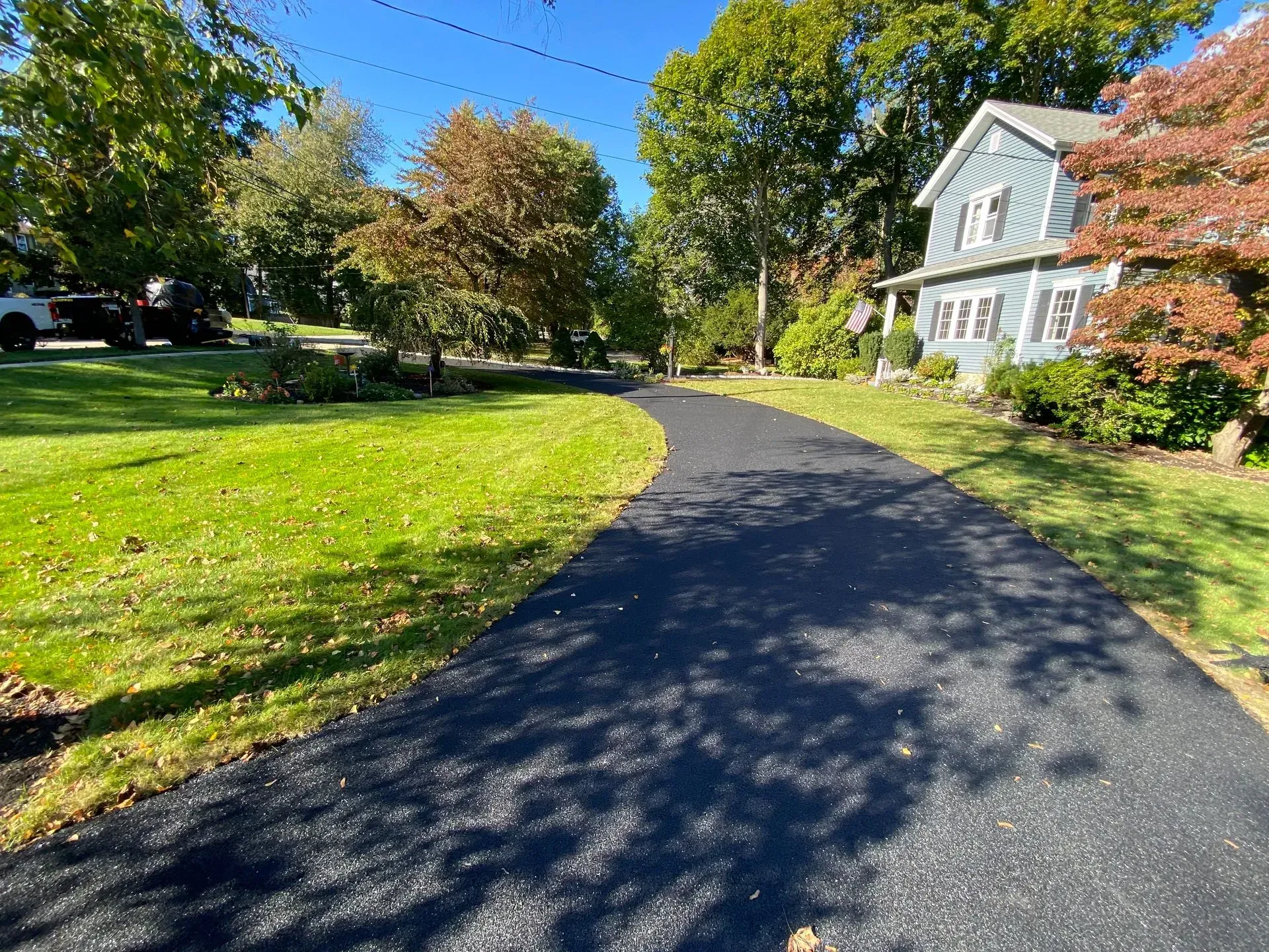 Newly paved black asphalt driveway winding through a grassy yard toward a blue house.