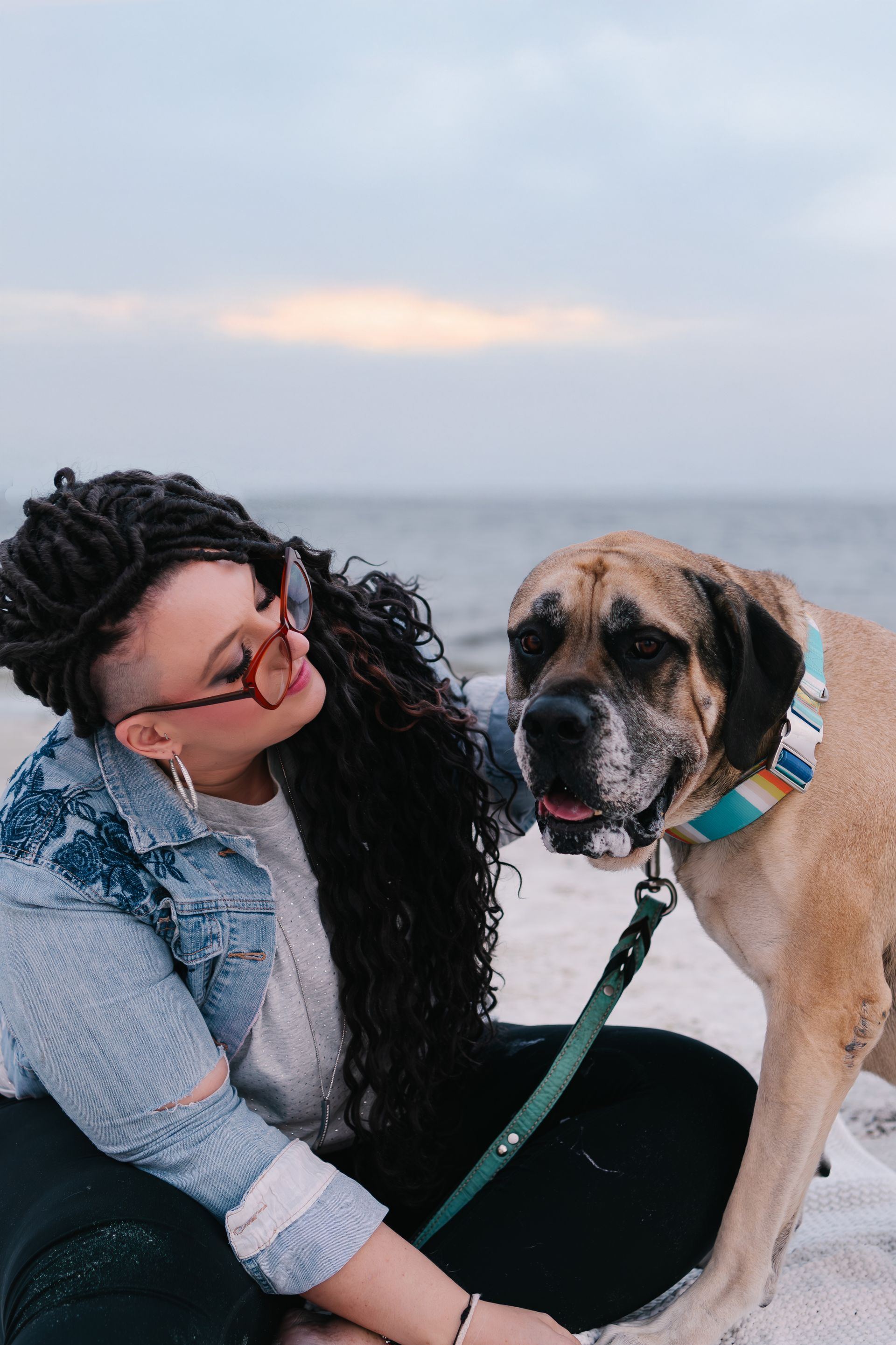 A woman is kneeling down next to a dog on the beach.