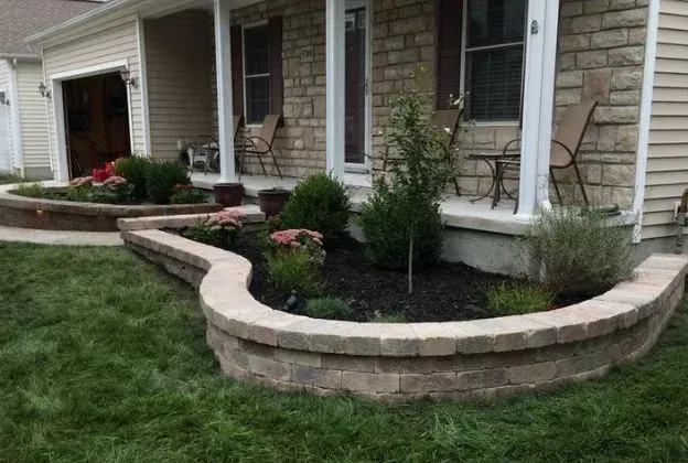 Front yard garden beds with stone retaining walls and shrubs along a house walkway