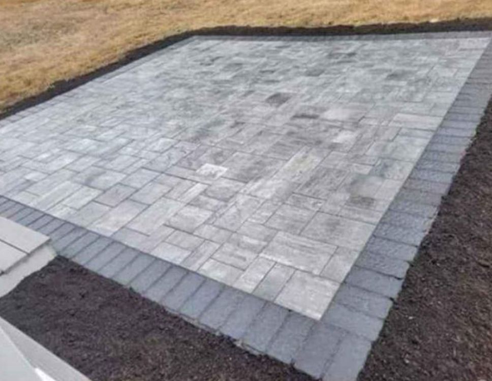 A newly paved gray stone patio bordered by darker edging stones in a yard