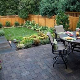 Backyard patio with black chairs and a table beside a landscaped lawn and wooden fence