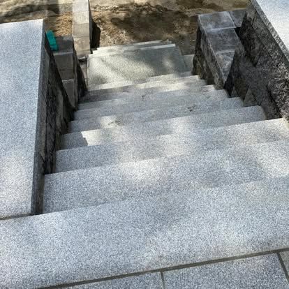 Concrete outdoor stairs between stone walls, leading down to a lower landing.