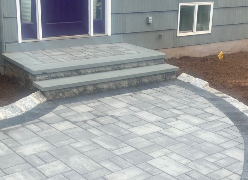 Front steps leading to a house entrance, with a gray stone paver patio and curved walkway.