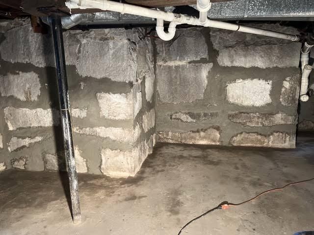 Dim crawlspace with concrete block support walls, exposed pipes, and a dirt floor.
