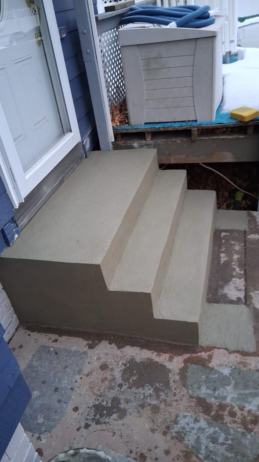 Concrete steps and ramp beside a door, with a raised platform and a covered appliance on top.