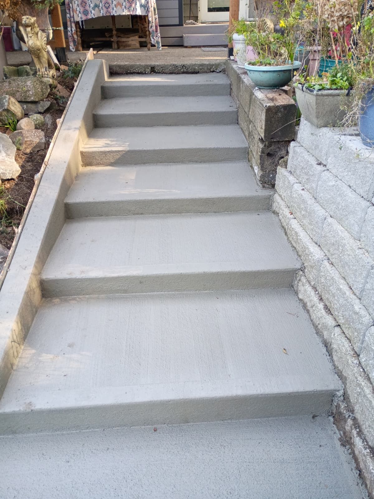 Concrete outdoor stairs leading to a porch, bordered by stone walls and potted plants