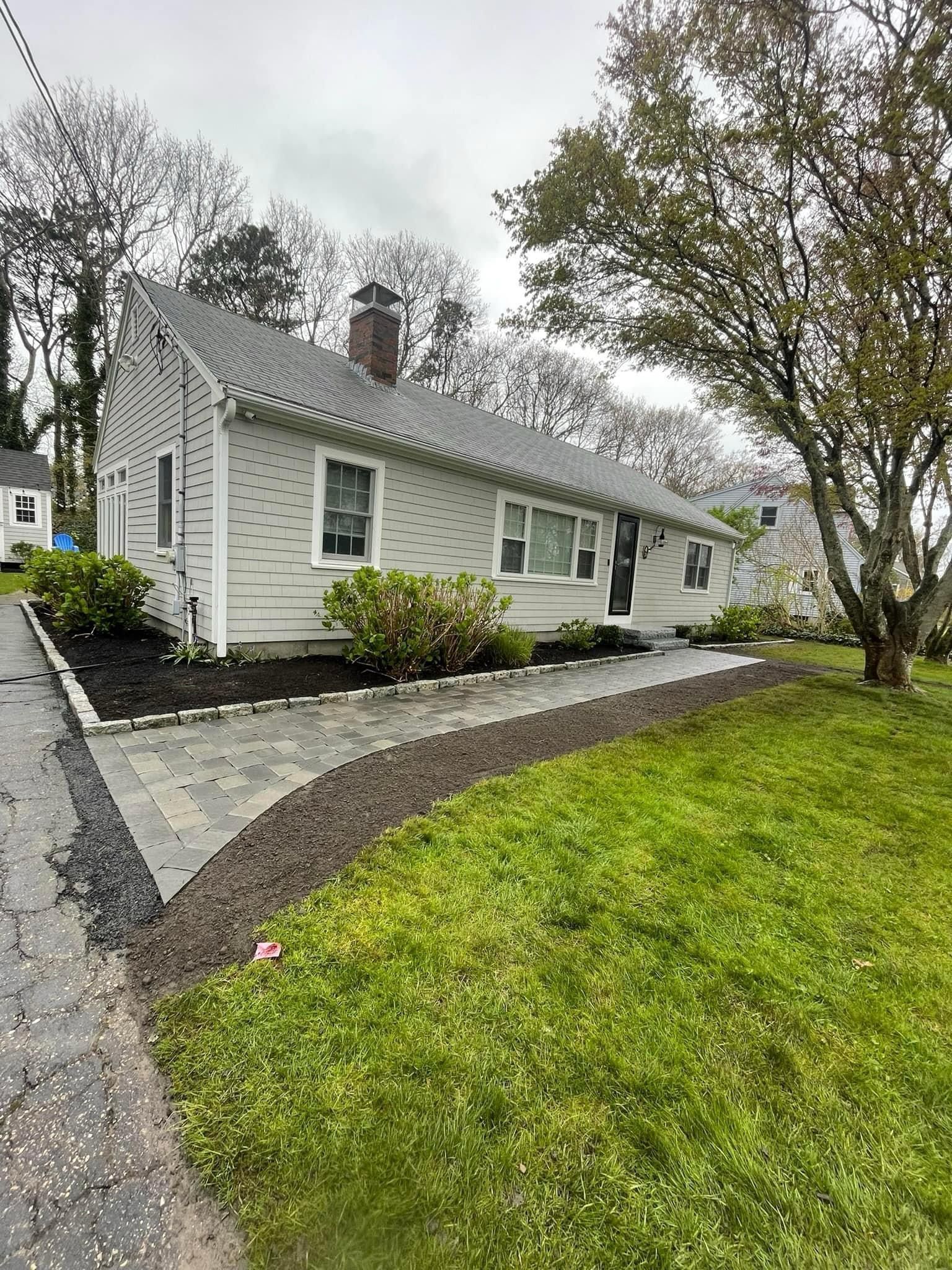 Single-story white house with gray roof, black shutters, and a landscaped front yard with trees and lawn.
