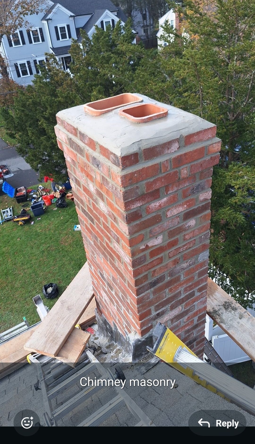 Brick chimney with copper cap on a house roof, seen from above with a yard and people below