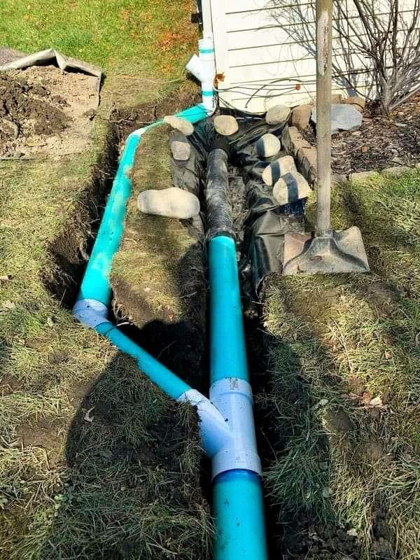 Blue drainage pipes and black tubing running along a house foundation in a grassy yard