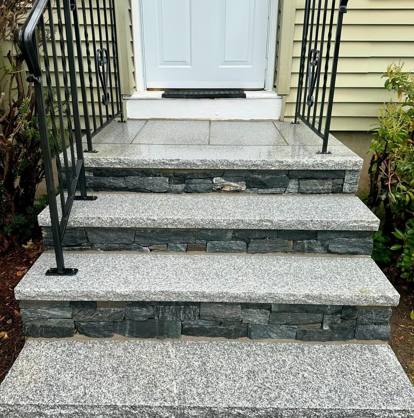 Front steps of a house with stone treads, black railings, and a white door at the top.
