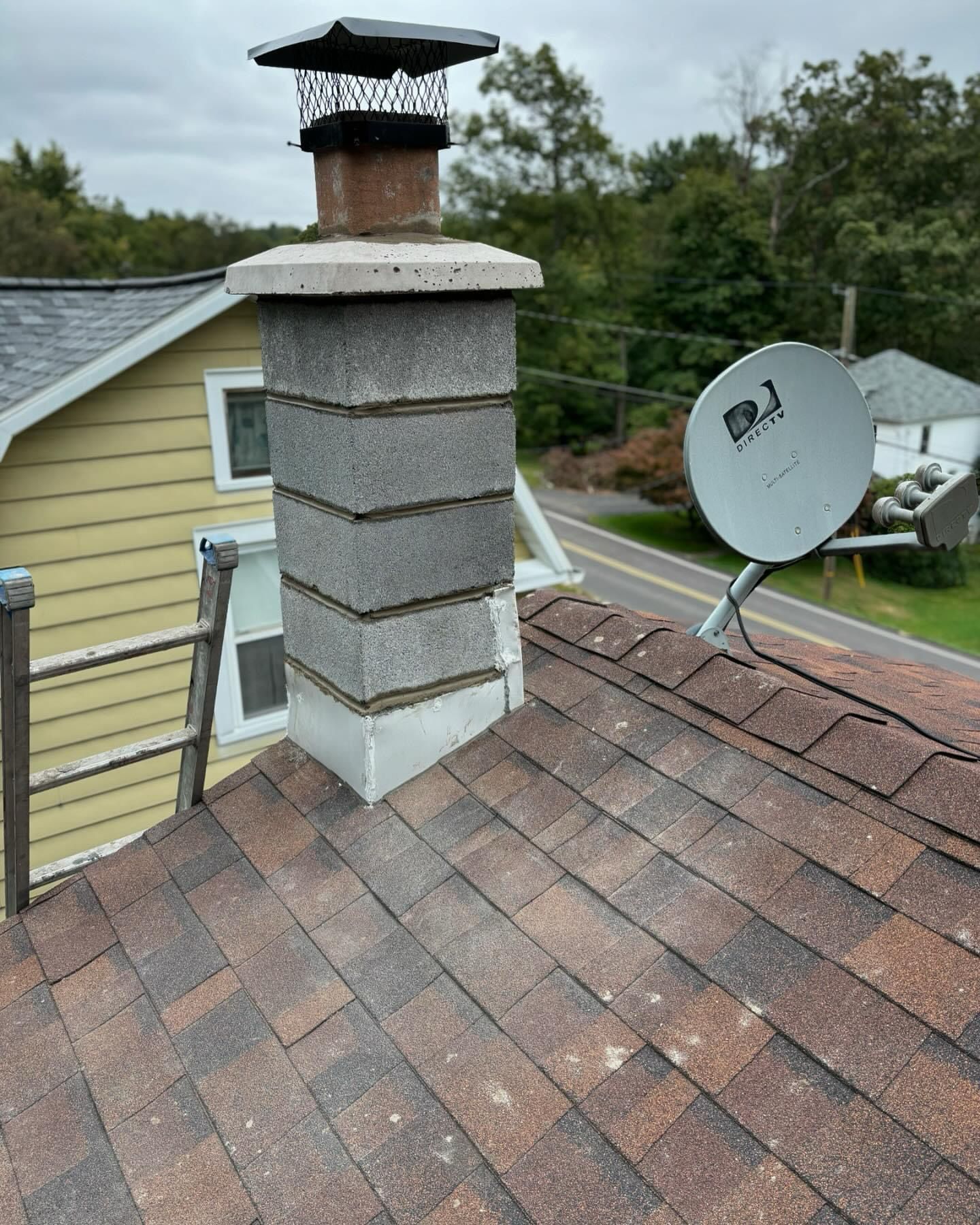 Roof with gray chimney and cap, brown shingles, and a satellite dish on a residential home.