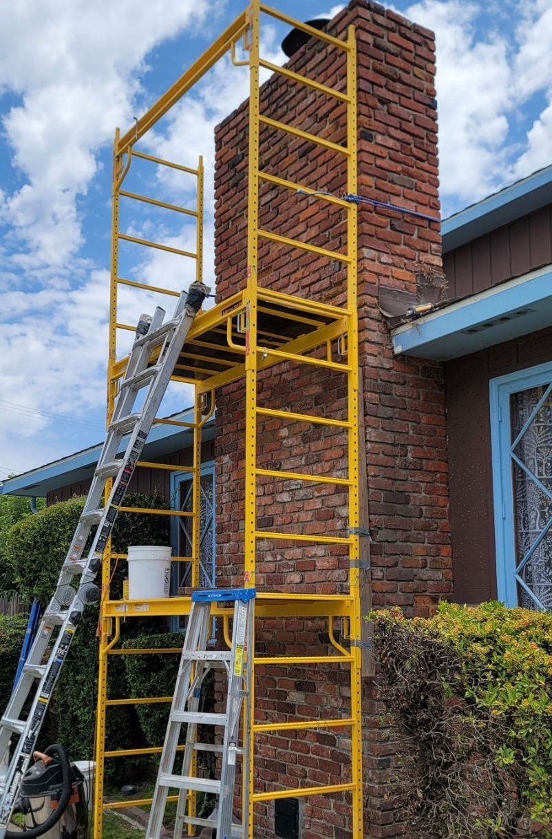 Yellow scaffolding and ladders beside a brick house chimney under repair