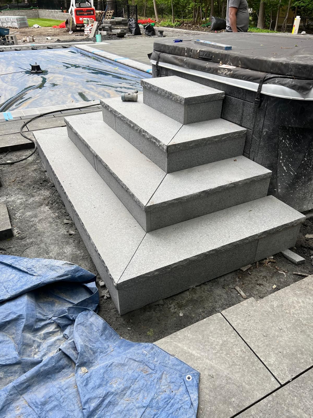 Gray stepped concrete platform under construction beside a walkway, with tools and tarps nearby