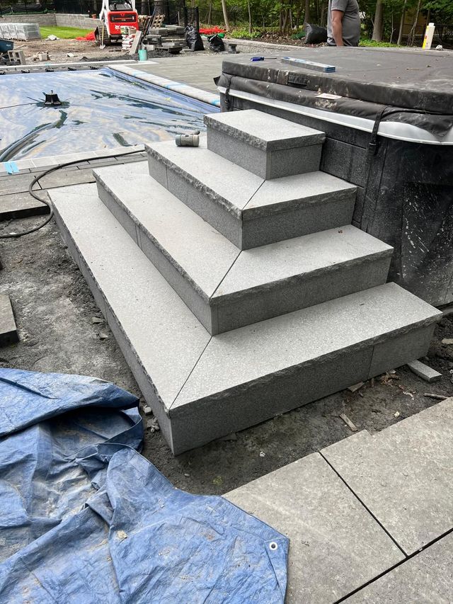 Gray stepped concrete platform under construction beside a walkway, with tools and tarps nearby