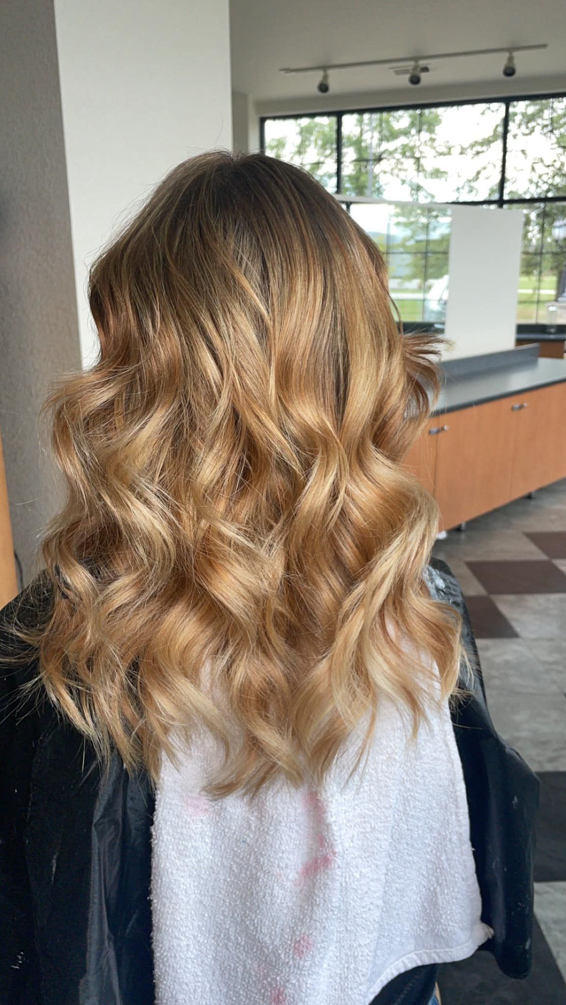 a woman with long wavy blonde hair is getting her hair cut in a salon .