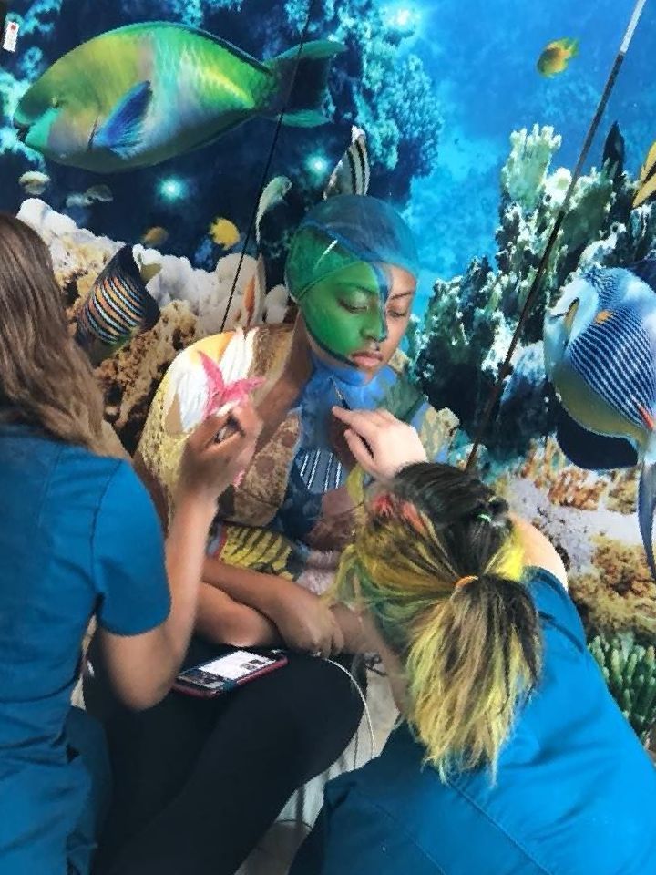a woman is getting her face painted in front of a picture of fish