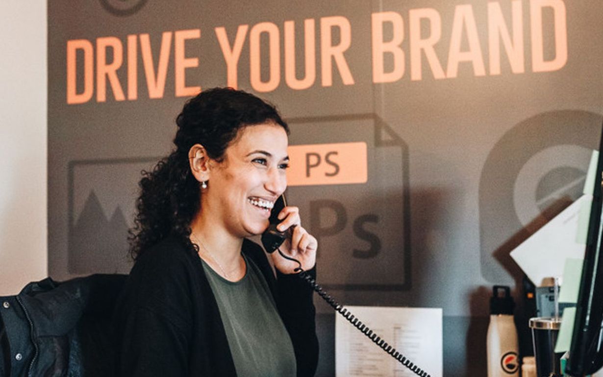 Woman smiles while talking on a phone at a desk. 