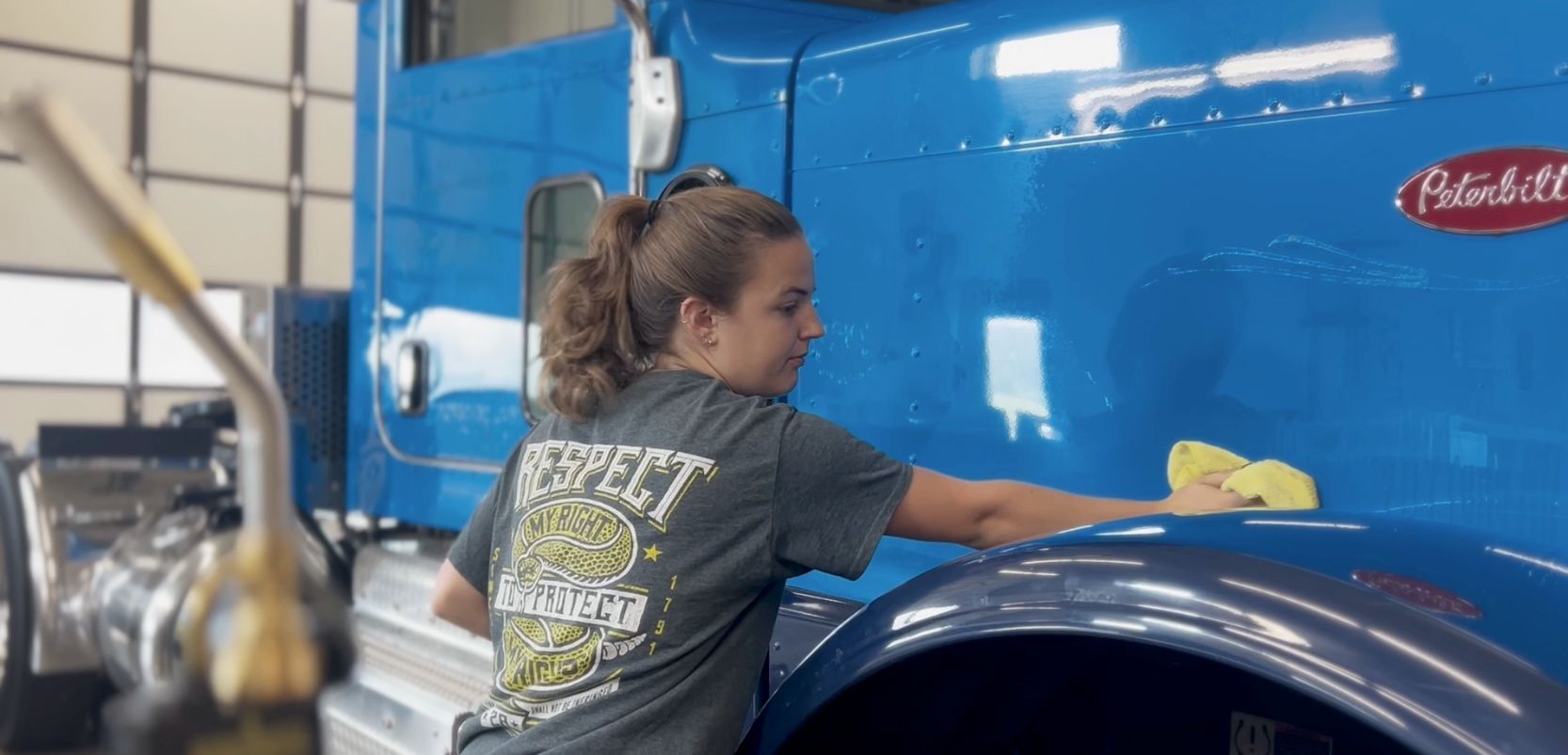 A person washes the blue exterior of a semi-truck. A Peterbilt logo is visible on the truck.