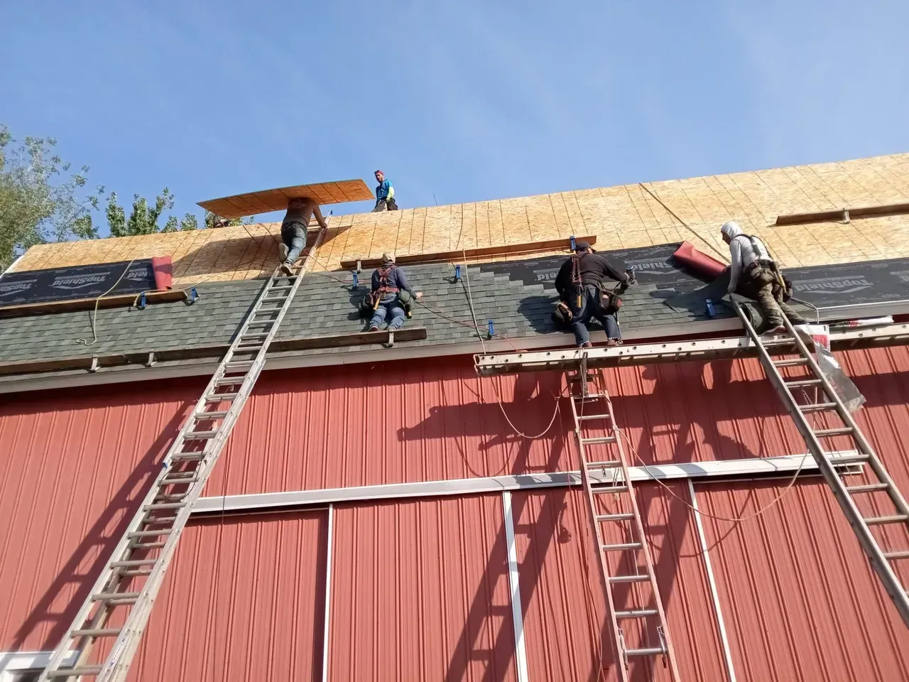 A group of men are working on the roof of a red barn