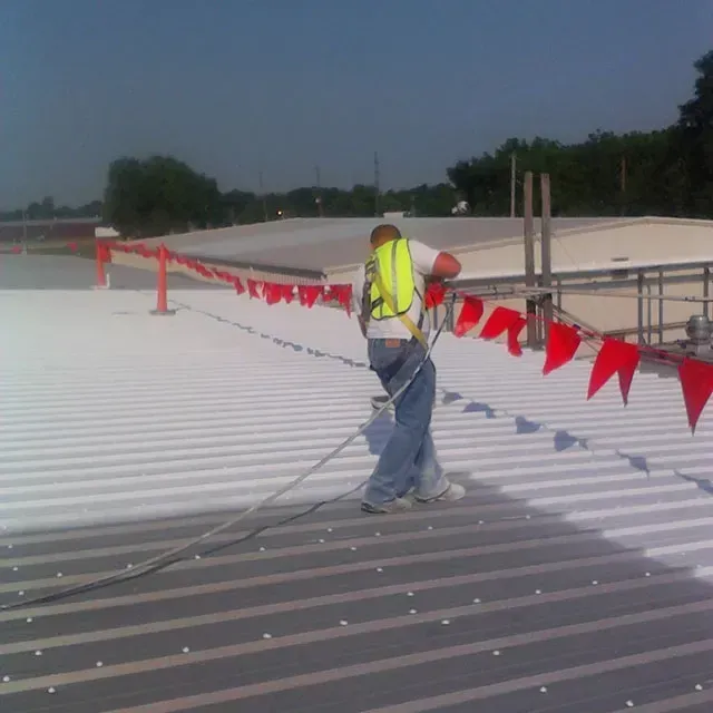 A man is spraying white paint on a roof