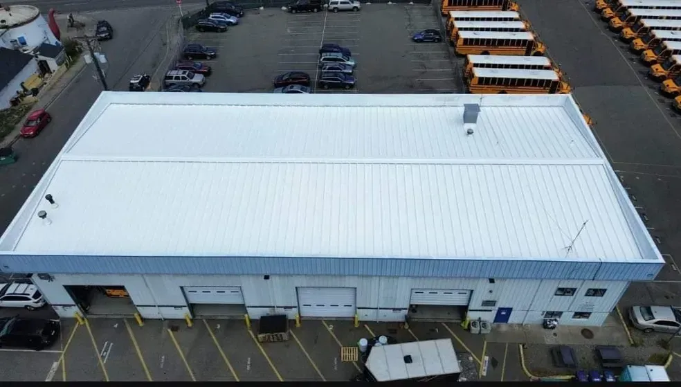 An aerial view of a building with a white roof and school buses parked in front of it.