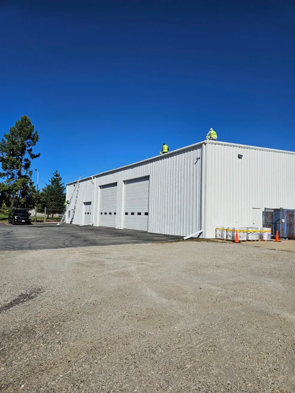 A large white building with a lot of garage doors is sitting on top of a gravel lot.