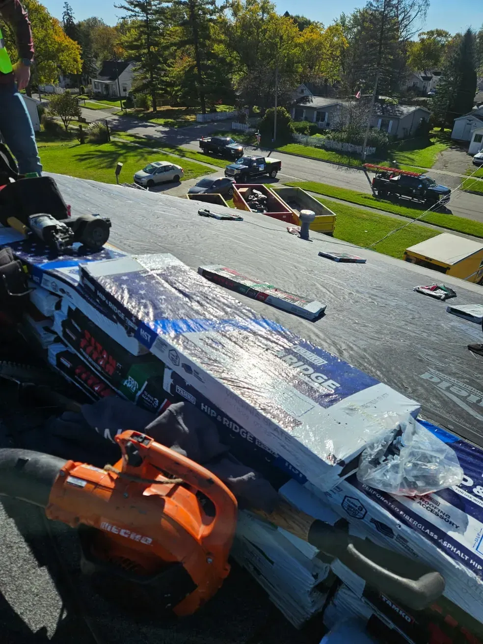 A blower is sitting on a roof next to a box of roofing shingles