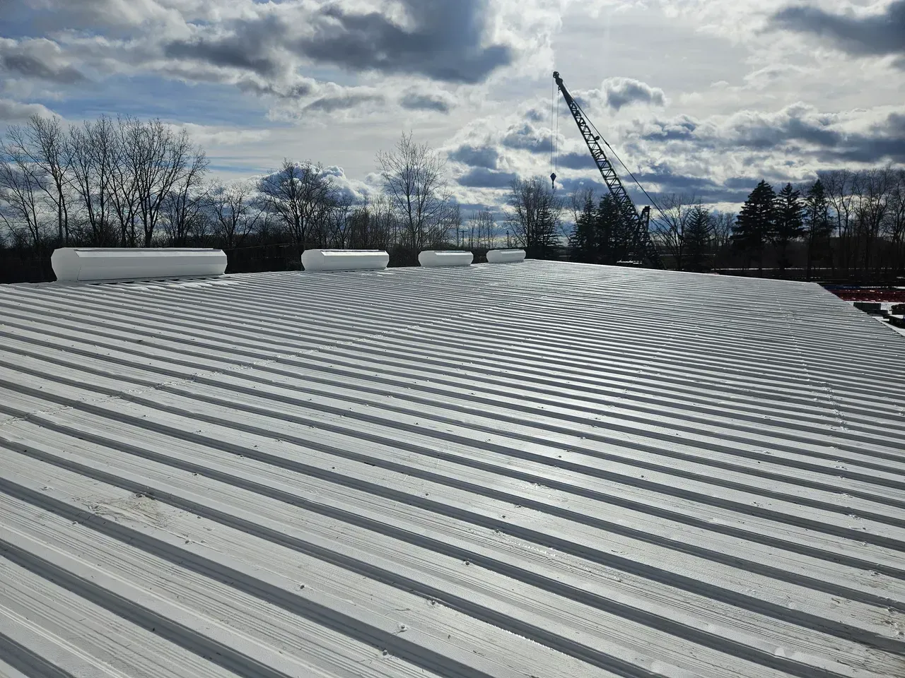 A metal roof with a crane in the background on a cloudy day.