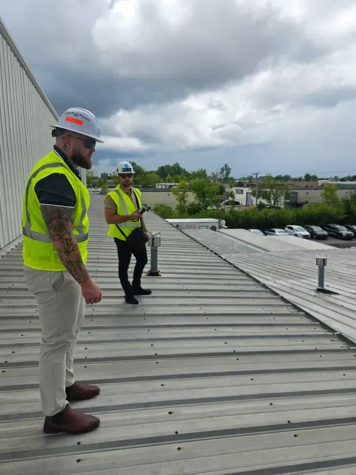 Two construction workers are standing on top of a roof.