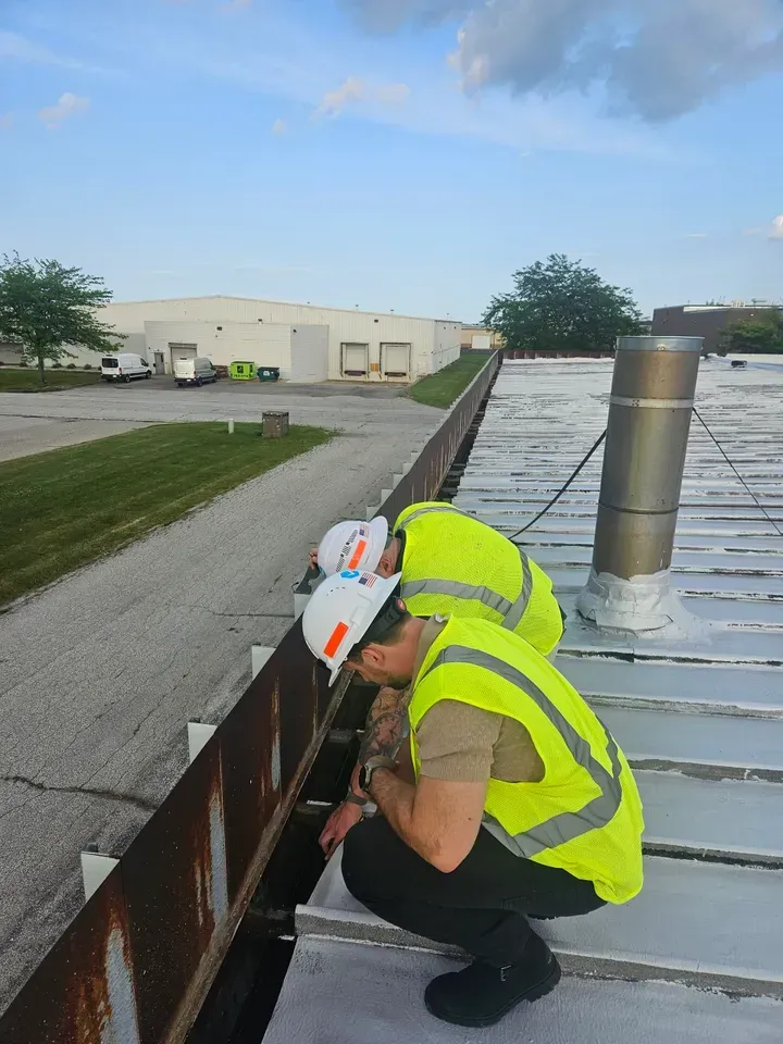 Two men in yellow vests and hard hats are inspecting a roof