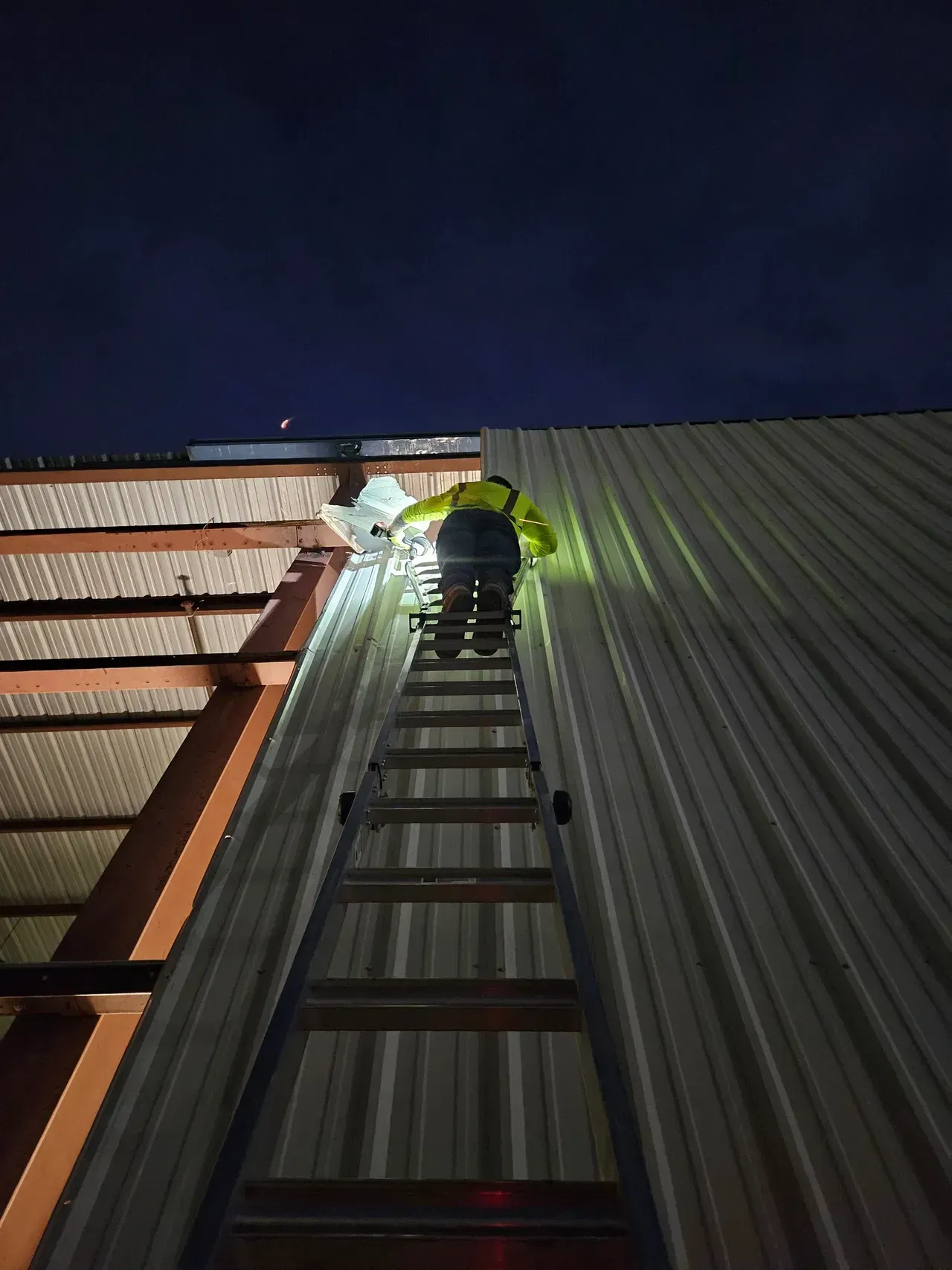 A man is standing on a ladder on top of a building at night.