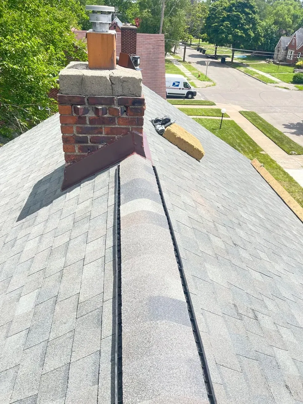 A roof with a chimney on it and a mail truck in the background.