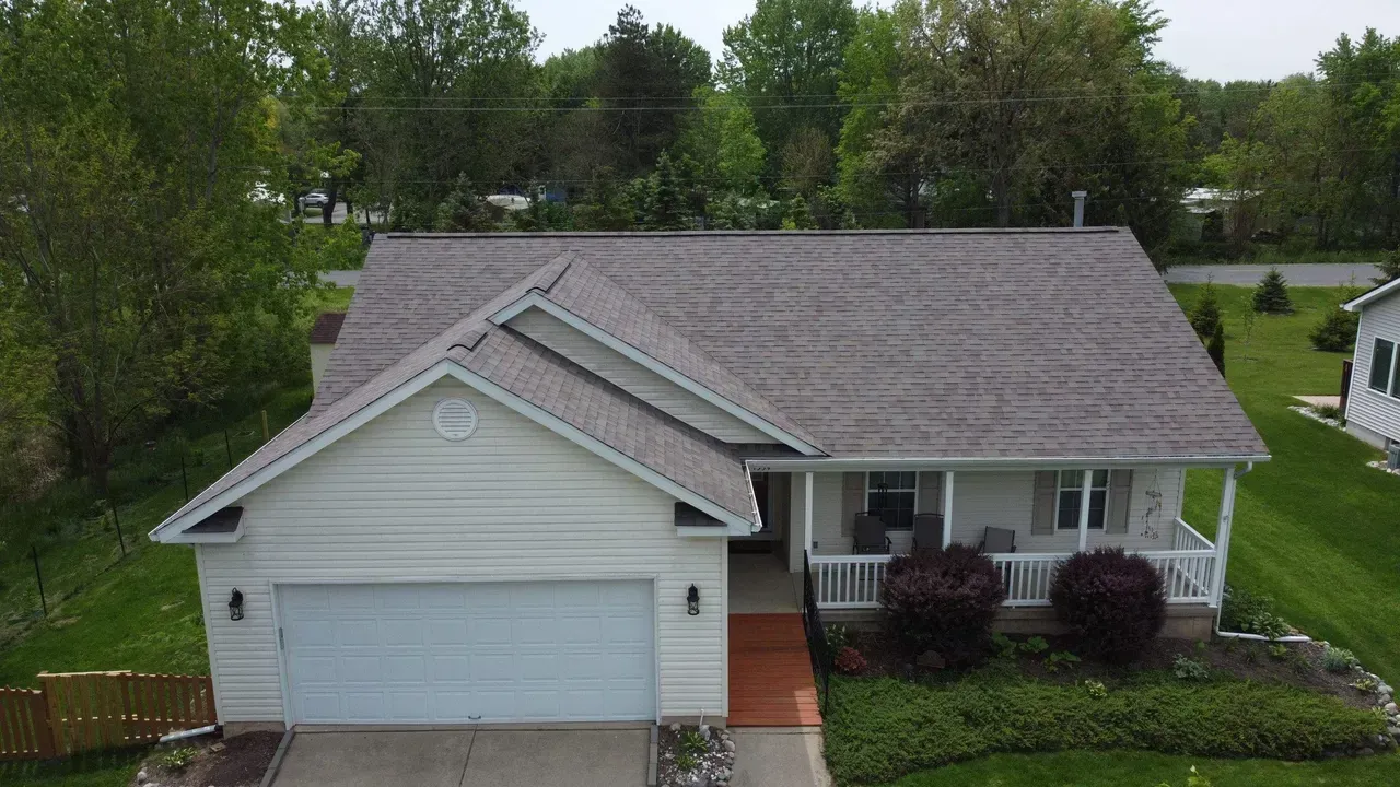An aerial view of a white house with a gray roof and a porch.