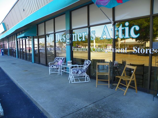 The storefront of My Designer's Attic, a furniture consignment store, with patio chairs and tables on the sidewalk.