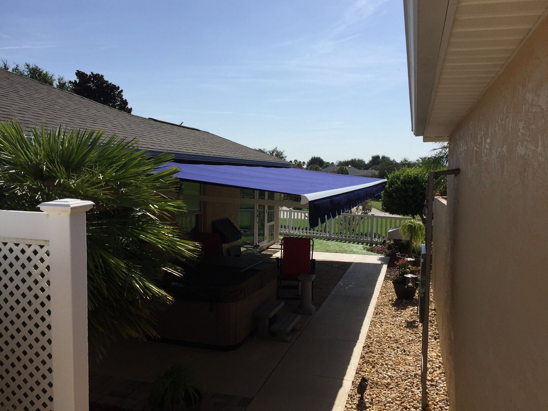 A blue retractable awning extended over a patio area between two houses on a sunny day.