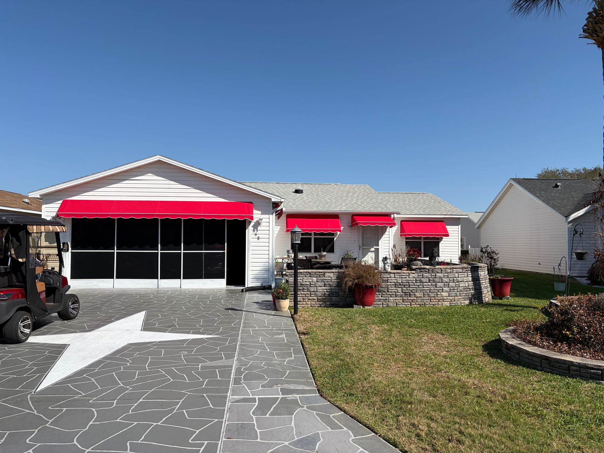 A one-story suburban home with red fabric awnings over the windows, a stone patio, and a driveway with a painted white star.