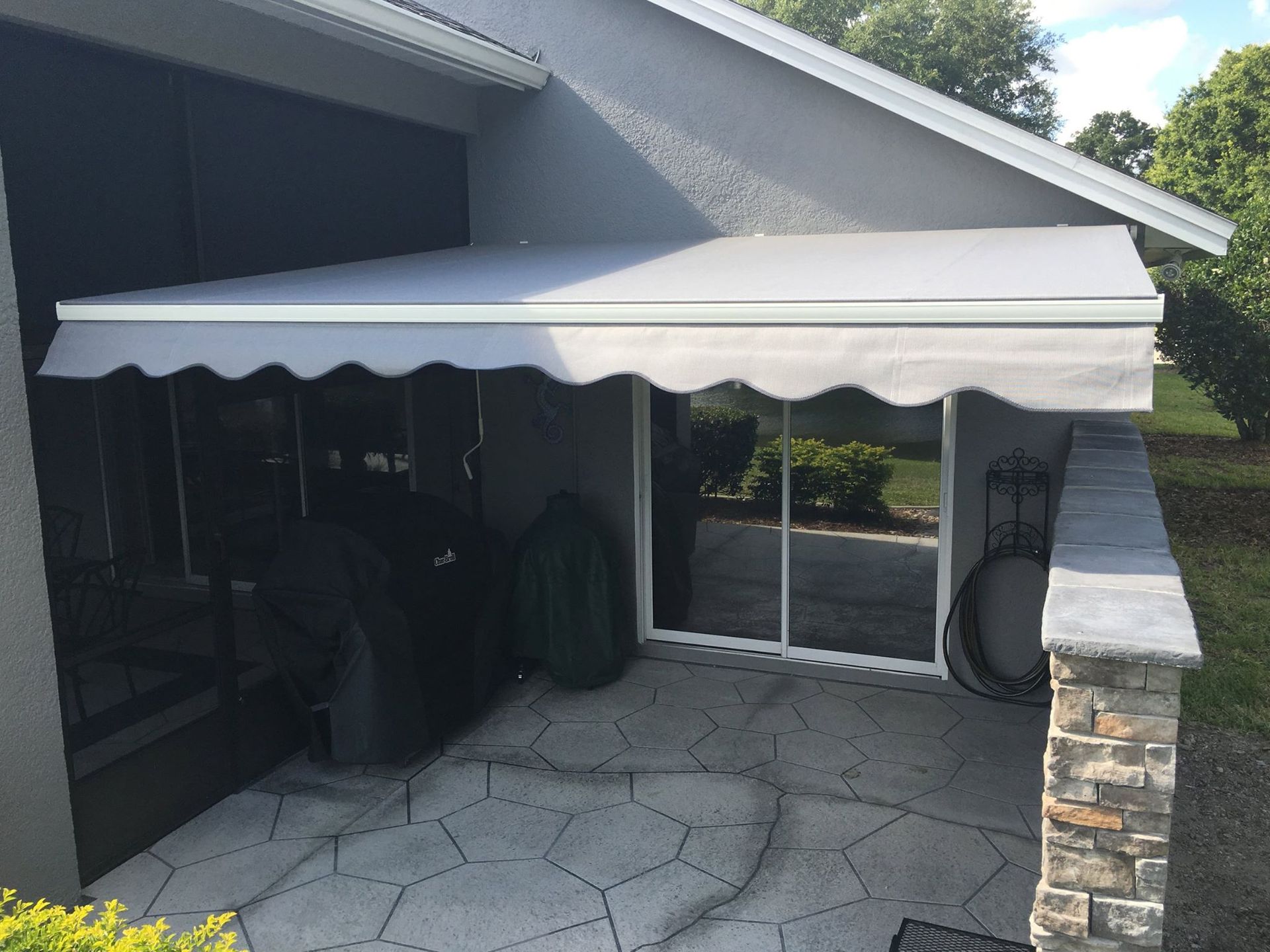 A light gray, scalloped-edge retractable awning mounted over a sliding glass patio door on a gray house exterior.