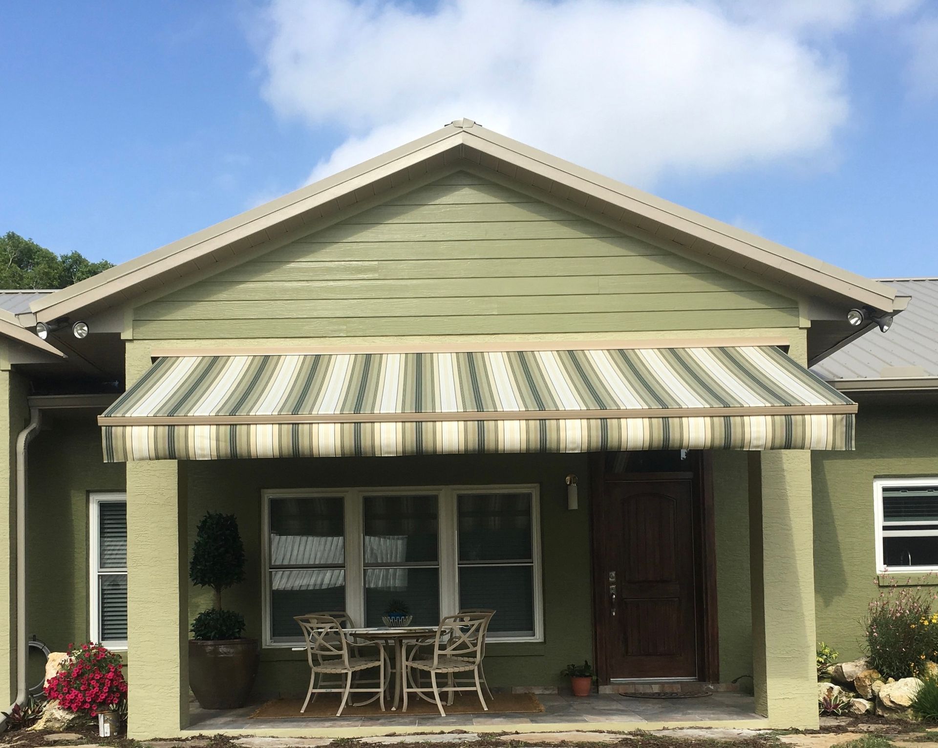 A house exterior with installed grey retractable privacy screens on a patio, featuring a stone path and landscaped mulch.