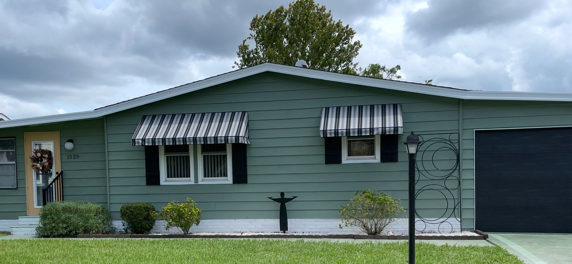 A light-yellow house exterior with three windows featuring striped fabric awnings and dark brown shutters.