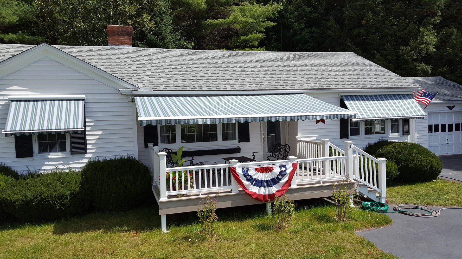 A white, single-story house with a porch featuring a patriotic red, white, and blue decoration and striped awnings.